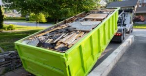A lime green dumpster full of debris from a home renovation is loaded onto a truck in a home driveway.